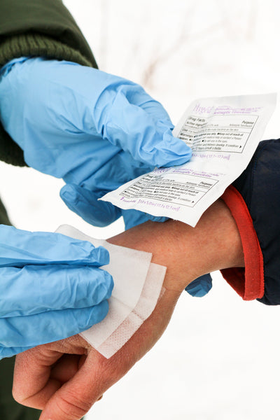 Antiseptic Wipes being applied to skin by medical professional wearing blue nitrile gloves, demonstrating proper wound cleaning technique with medical documentation visible in background