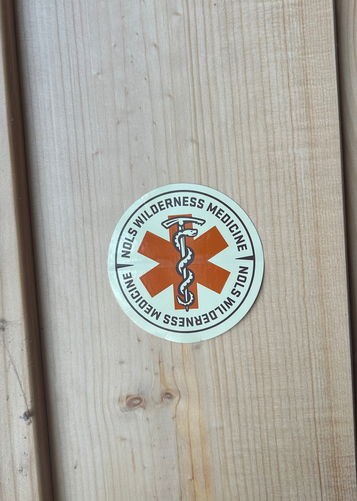 Round sticker with 'Wilderness Medicine' text and logo on a wooden surface