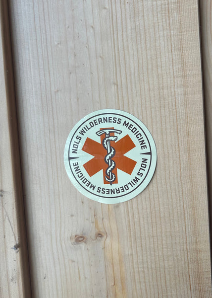 Round sticker with 'Wilderness Medicine' text and logo on a wooden surface
